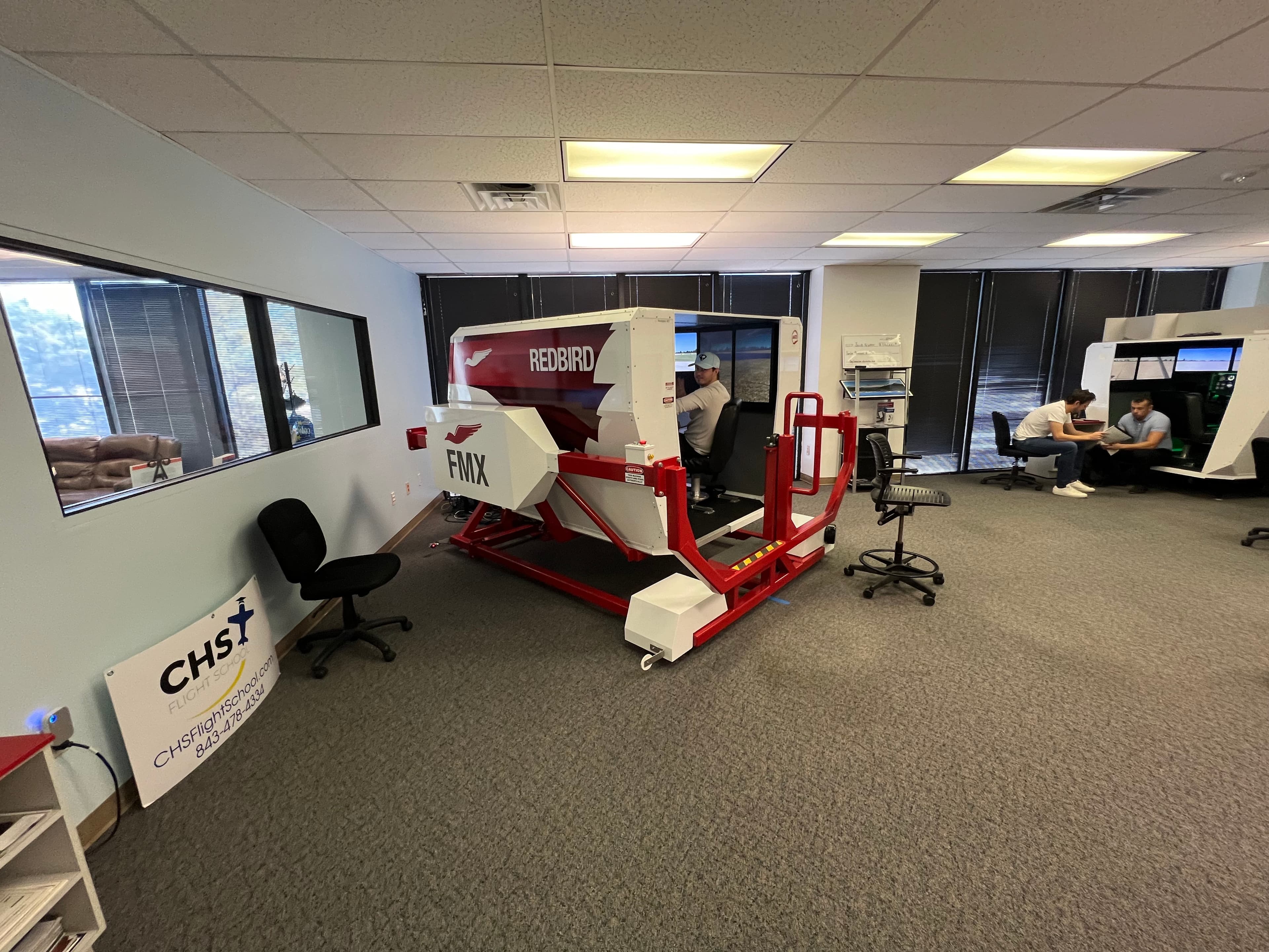Student pilot using a Redbird FMX flight simulator in a flight school training facility.