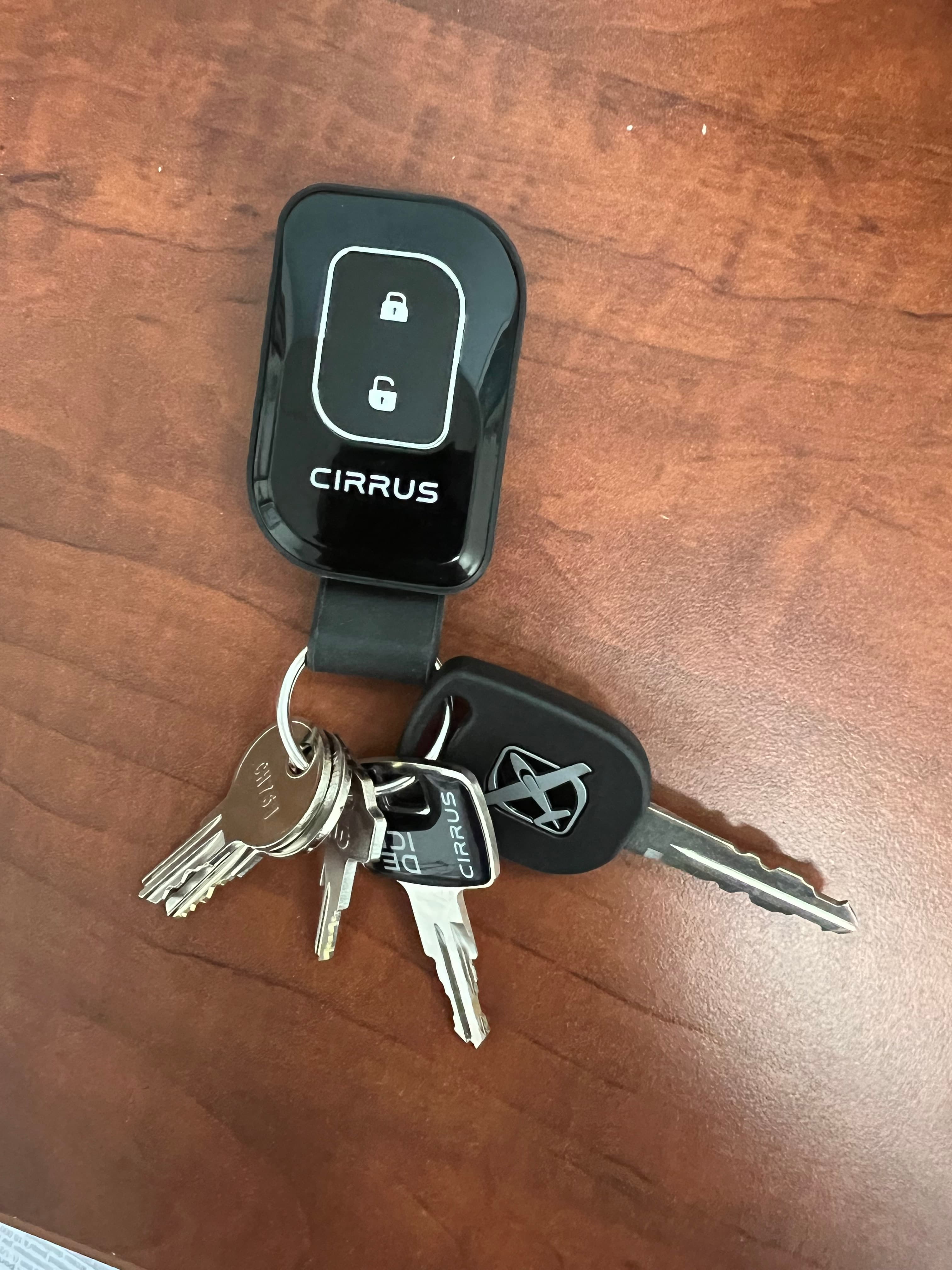 Black Cirrus aircraft key fob and metal keys on a brown wooden table surface.