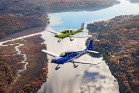 Blue and yellow small planes flying in formation over a river and autumn forest.