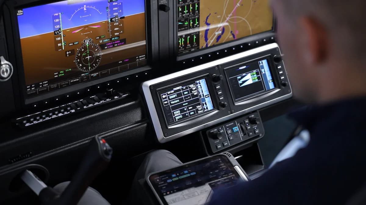Pilot operating a modern glass cockpit with digital flight displays and a navigation tablet.
